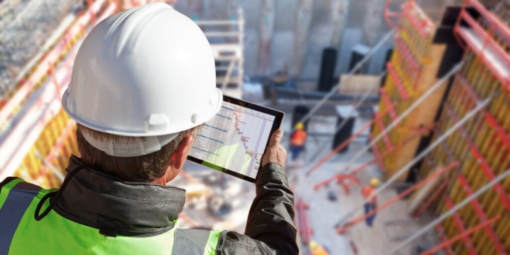 Profissional de construção civil usando tablet para monitorar sistemas de automação e despoeiramento em obra industrial.